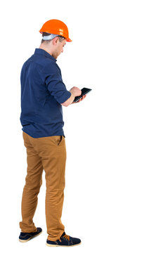 Backview of business man in construction helmet stands and enjoys tablet or using a mobile phone. Standing young guy. Rear view people collection.  backside view of person.  Isolated over white
