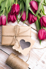 Fototapeta na wymiar Gift box and tulips bouquet on white wooden background - retro style