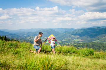 Dad and daughter launch a kite against the backdrop of beautiful views of mountains and sky. Horizontal