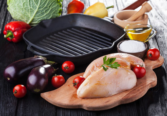 raw chicken fillets on wooden cutting board, with vegetables