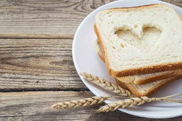 Sliced white bread on a plate with ears of wheat on a wooden tab