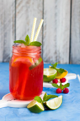 Raspberry lemonade with lemon, lime, mint and ice in the glass on the blue background