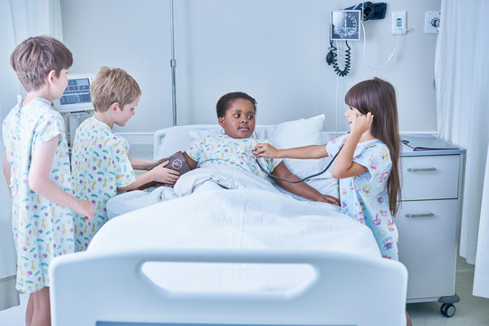 Girl and boy patients playing at treating friend in bed on hospital children's ward