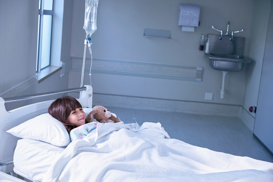 Girl patient in bed hugging toy rabbit on hospital children's ward