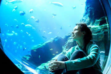 Young pretty woman watching fishes in a tropical aquarium