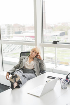 Bored mature businesswoman with feet up on office desk