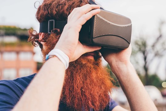 Young male hipster with red hair and beard wearing virtual reality headset