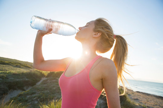 Young woman at beach, drinking from water bottle
