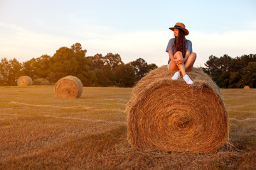 Naklejka na ściany i meble Pretty young woman sitting on a hay bale.