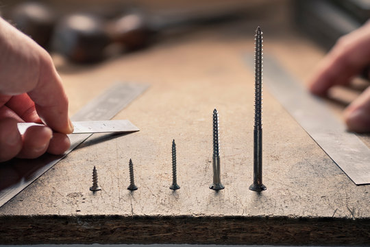 Hand holding ruler, screws standing in a row in ascending order