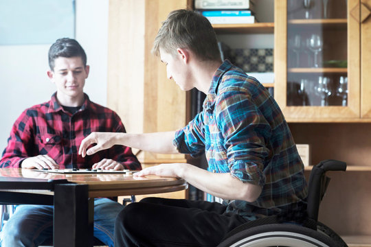 Young man using wheelchair playing draughts with friend in kitchen
