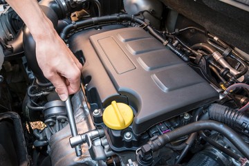 Hand repairing a modern car engine with a wrench