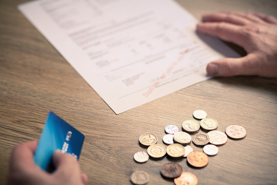 Mans hands holding credit card with coins and bill on table