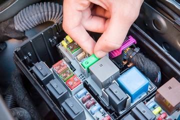 Hand checking a fuse in the fuse box of a modern car engine