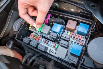 Hand checking a fuse in the fuse box of a modern car engine