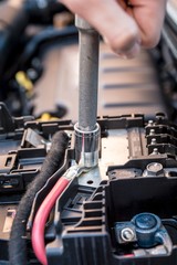 Hand checking the bolt of the battery with a wrench in a modern car engine