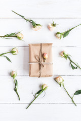 Gift and roses on wooden white background. Top view, flat lay
