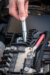 Hand checking the bolt of the battery with a wrench in a modern car engine