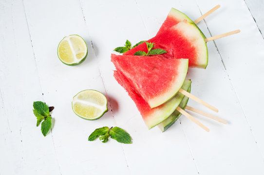 Watermelon slice popsicles and lime on rustic wood background