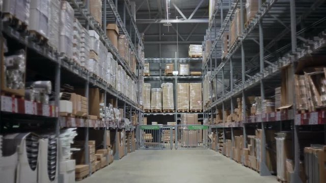 Camera moves between palettes with cardboard boxes and different materials in a storage warehouse