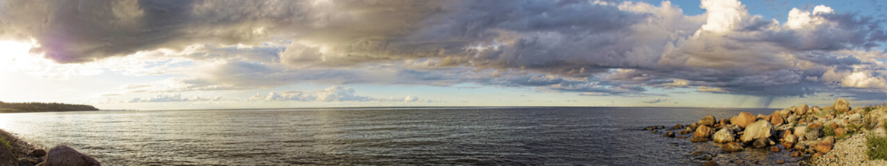 Seascape wide panorama with sunset and clouds. Stones and pebbles on the shore.