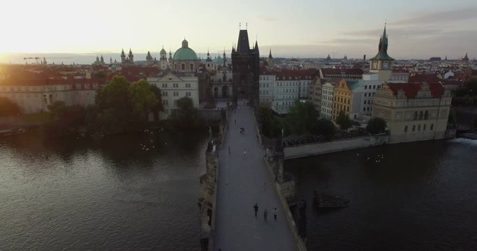 Aerial camera flies backwards along the Charles Bridge towards the Old Town of Prague. Shot at Dawn