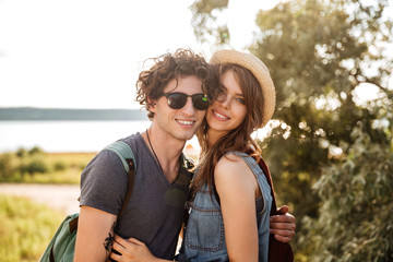 Portrait of smiling hipster couple standing against trees and sea