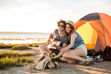 Couple playing guitar and frying marshmallows on bonfire together