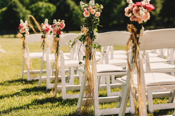 Ropes which hold pink bouquets on white chairs hang from them