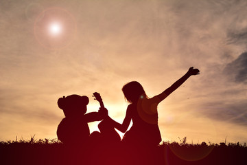 Fototapeta premium Silhouette girl playing musical with teddy bear at sunset