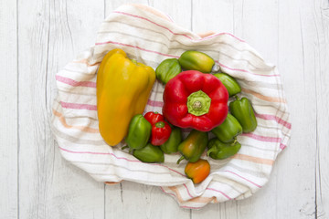 Peppers of different colors on a rustic cloth and wooden backgro