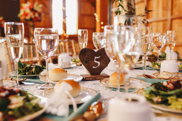 Wooden table number 5 stands between the plates with buns and gl