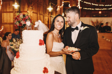 Bride smiles with wedding cake in her mouth while standing behin