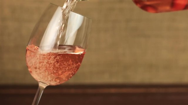 Rose wine pouring into glass on wooden table