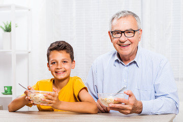 Grandfather and grandson are eating oatmeal at home. Healthy lifestyle.
