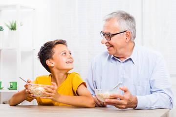 Grandfather and grandson are eating oatmeal at home. Healthy lifestyle.