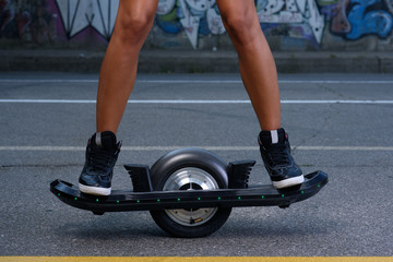 sporty athletic caucasian cute teen riding electric onewheel skateboard having fun in the street posing and hold in her hands