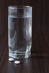 Pills and glass of water on dark background