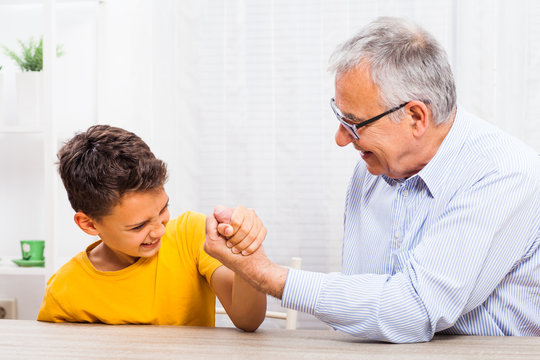 Grandfather and grandson arm wrestle at home.