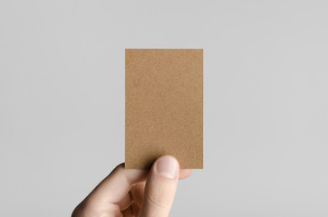 Kraft Business Card Mock-Up (85x55mm) - Male hands holding a kraft card on a gray background.