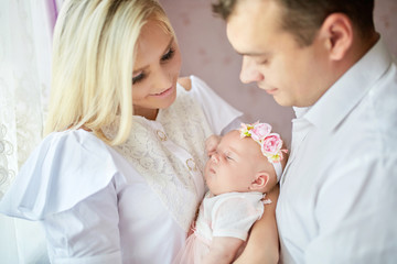 Mom and dad admire their little girl while holding her in their