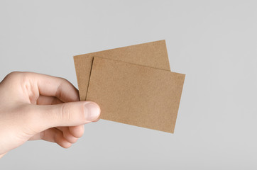 Kraft Business Card Mock-Up (85x55mm) - Male hands holding kraft cards on a gray background.