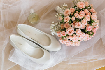 Delicate pink bouquet lies behind white shoes on the veil