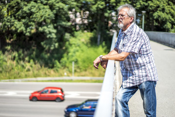 Mann mit Brille blickt kritisch von der Brücke auf die Autobahn