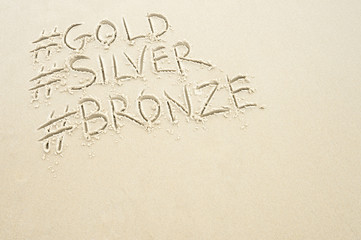 Hashtag social media message for gold, silver, and bronze medals, sport's first, second, and third place, written in sand on the beach in Rio de Janeiro, Brazil