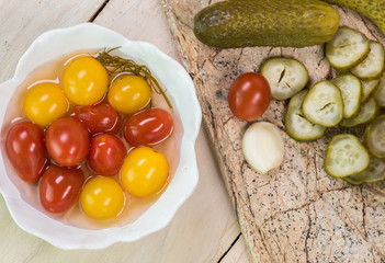Pickles on a cutting board and bowl with cherry tomatoes pickles