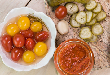 Dill pickles and cherry tomatoes pickles on a cutting board and roasted red pepper in open jar.