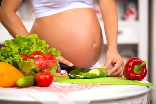Close-up of a pregnant belly. Pregnant woman in the kitchen preparing a vegetable salad.
