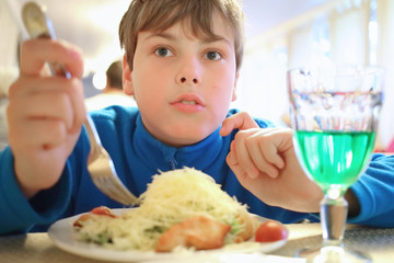 Portrait of a boy with a big portion of salad and green drink in the cafe