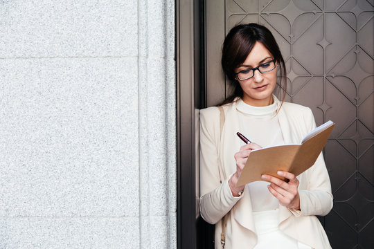 Stylish businesswoman in glasses writing in notebook